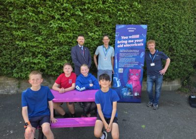Picture of students and headteacher of Temple Ewell Primary School receiving their prize of a pink recycled plastic picnic table from Rich and Rob of the e-Waste Warriors team